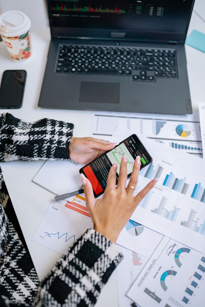 Mastering the First Impression: Your intriguing post title goes here Person analyzing business charts with smartphone and laptop on desk.